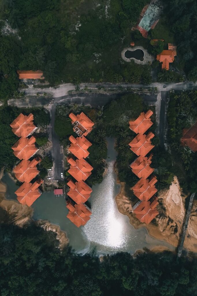 Top view complex of similar cottages with red roofs built on sandy shore of small pond in tropical countryside
