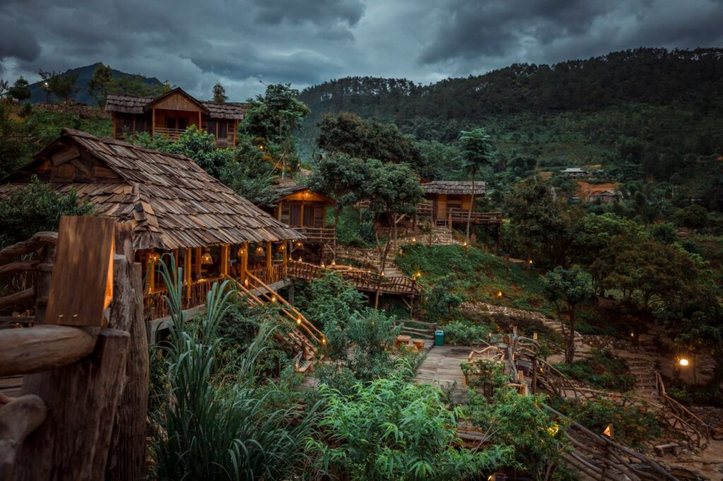 Scenic view of rustic wooden cabins surrounded by lush greenery under a dramatic sky.