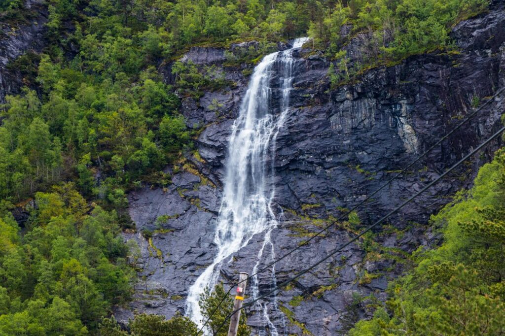 Captivating waterfall cascading down a rocky cliff surrounded by lush green forest in Hol, Norway.